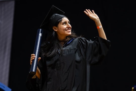 A graduating woman waves after accepting her diploma. 