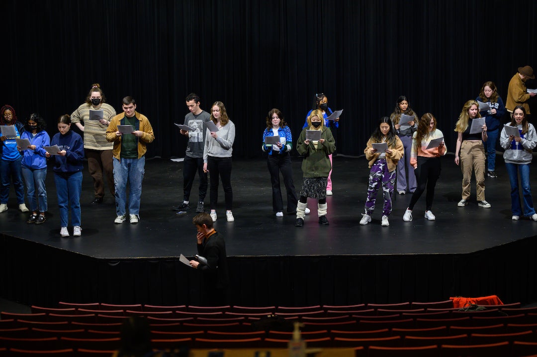 Professional actor stands in front of stage as students perform during workshop