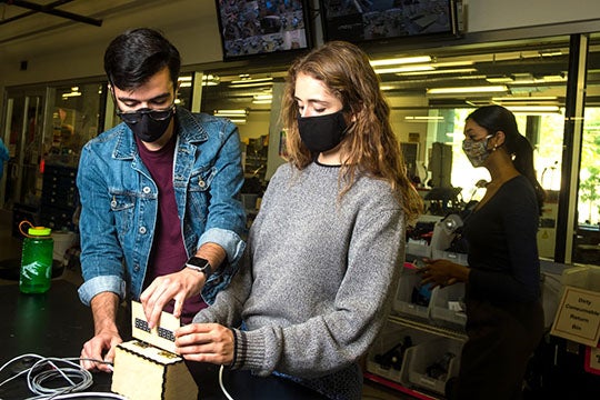Rice University engineering students have designed a low-cost touchless temperature monitor. Diego Gonzalez and Caterina Grasso Goebel make an adjustment to the temperature readout, attached by a long cable to the sensor to keep people at a distance. (Credit: Photo by Jeff Fitlow/Rice University)