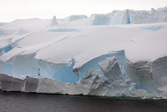 Blocks of dense, blue ice the size of convenience stores can be seen breaking away from Thwaites Glacier in a February 2019 photograph taken from the deck of the research vessel Nathaniel B. Palmer. (Photo by Linda Welzenbach)