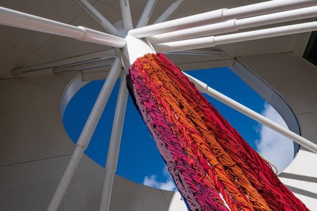 “The Questioning Column,” a rainbow-hued work by textile artist Sheila Hicks, is draped from the Moody’s towering oculus outside. (Photo by Jeff Fitlow)