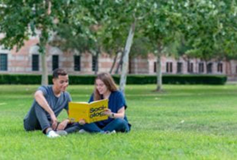 Students sitting on the lawn reading a book. 