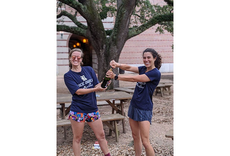 New Rice PhD grads Gisele Calderon and Shannon Carter pop a bottle of sparkling wine outside Valhalla.