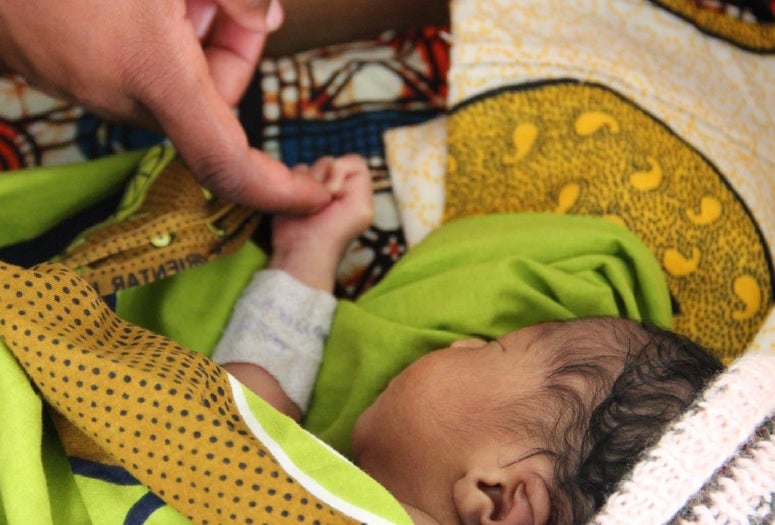 Caregiver touching newborn baby's hand