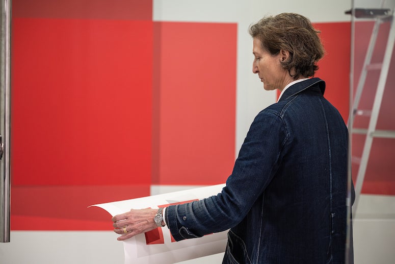 Artist Kate Shepherd oversees the installation of her new wall painting in the Jones Graduate School of Business. The painting is various shades of red in a series of intersecting planes.