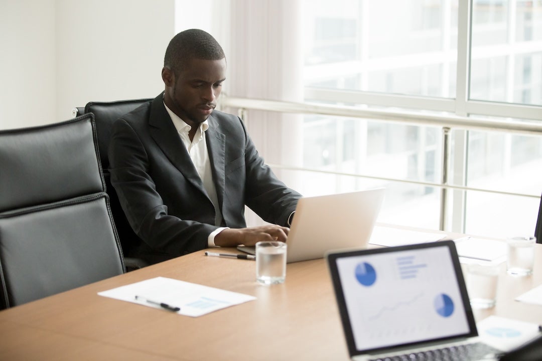 African American man sits at computer at a conference room table.