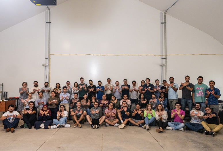 A group of about 30 Fulbright recipients and Rice administrators pose for a photo in the Grad Bubble making the "owls up" sympbol.