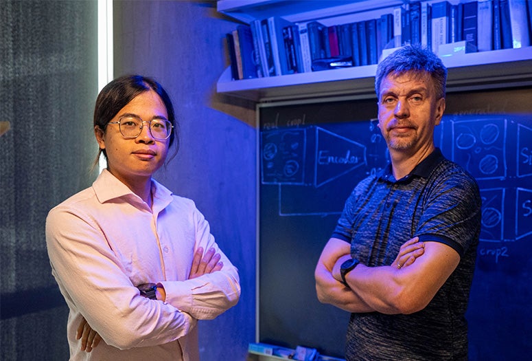 two researchers face the camera with arms crossed in front of a blackboard