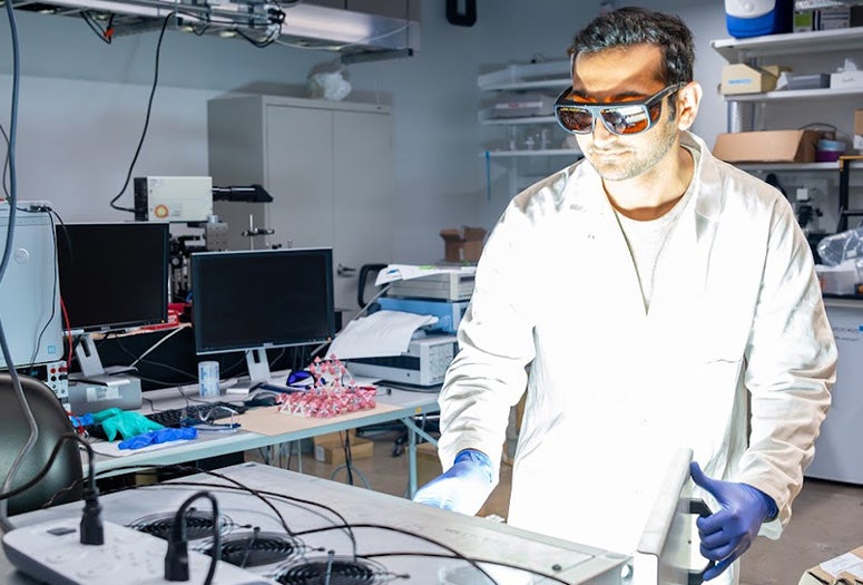 researcher in lab coat wearing gloves and protective glasses opens a device in a lab