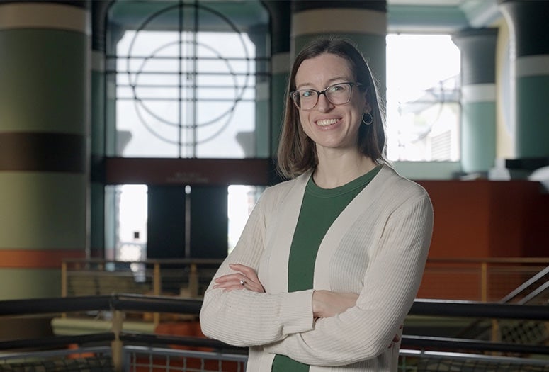 Woman in green shirt with white sweater with arms folded over her chest and smiling looks at the camera 