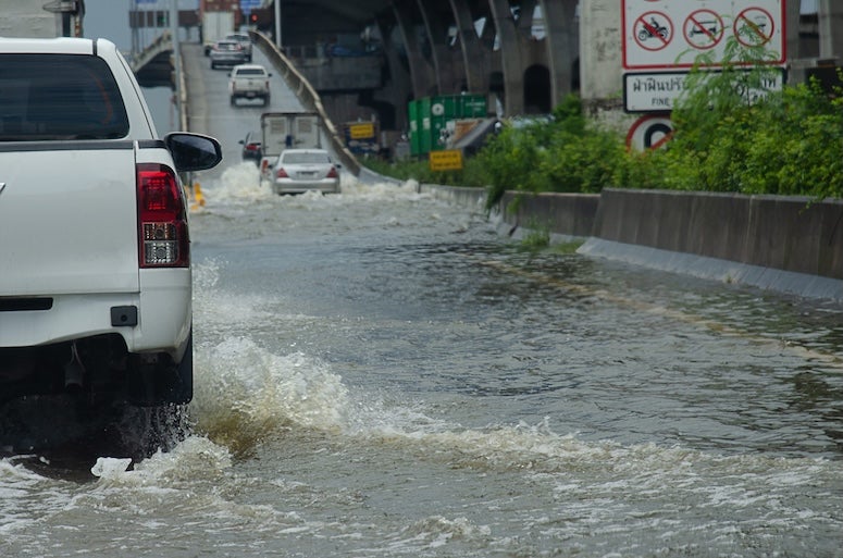 A truck drives through a flooded road, following a line of cars onto an elevated on-ramp