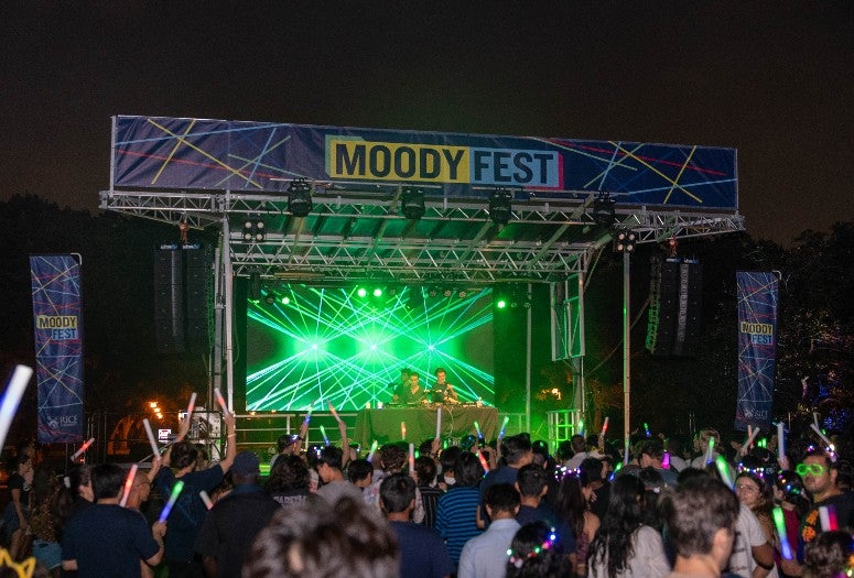A picture of the Moody Fest stage and all the attendees listing to music and waving glow sticks.