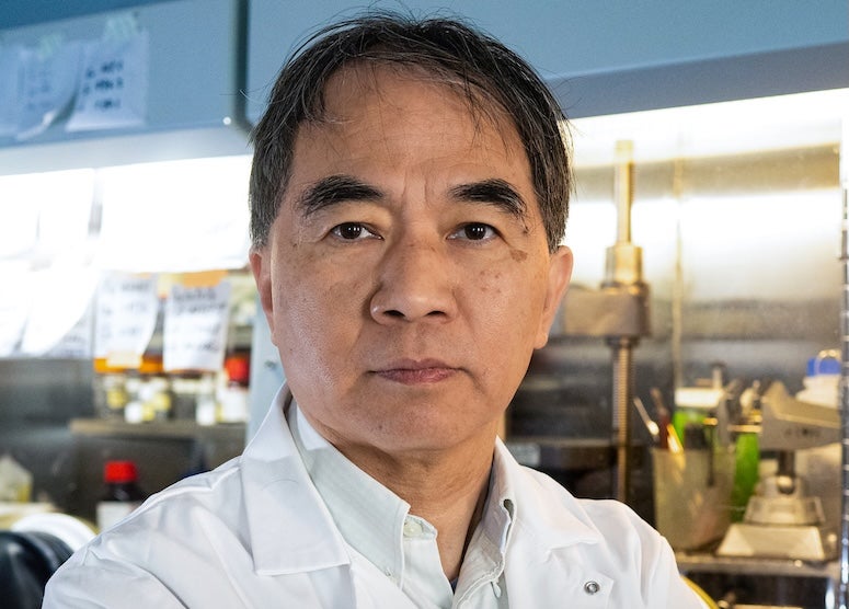 An Asian man in a lab coat stares confidently at the camera. 