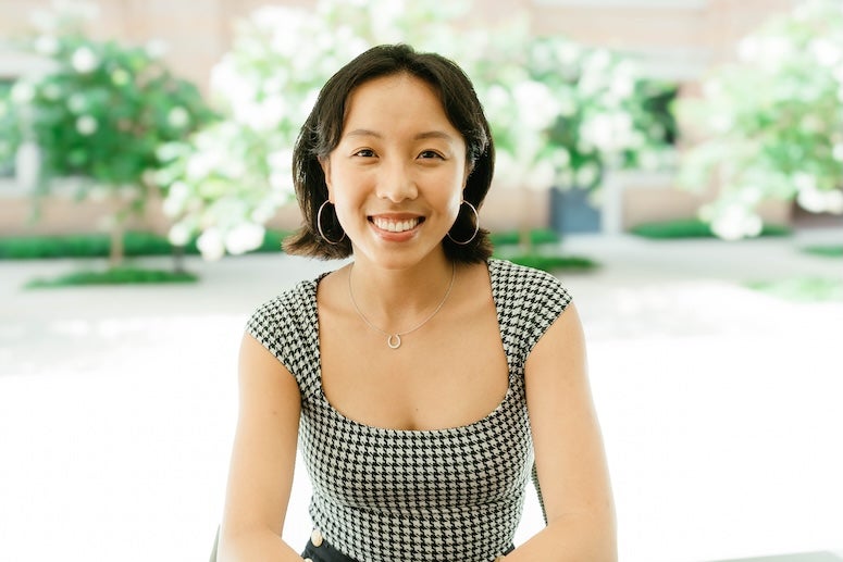 Lily Lee, sitting outside in front of green trees. 