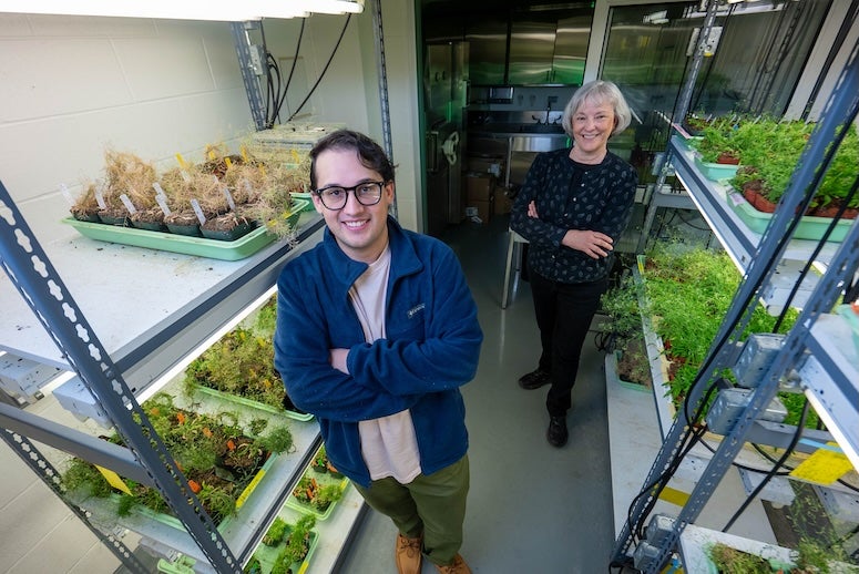 A young white man and older white woman stand in between shelves of plants