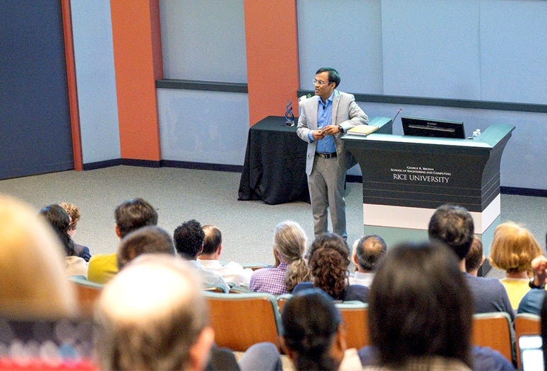 man in light gray suit standing next to lectern in front of a seated audience