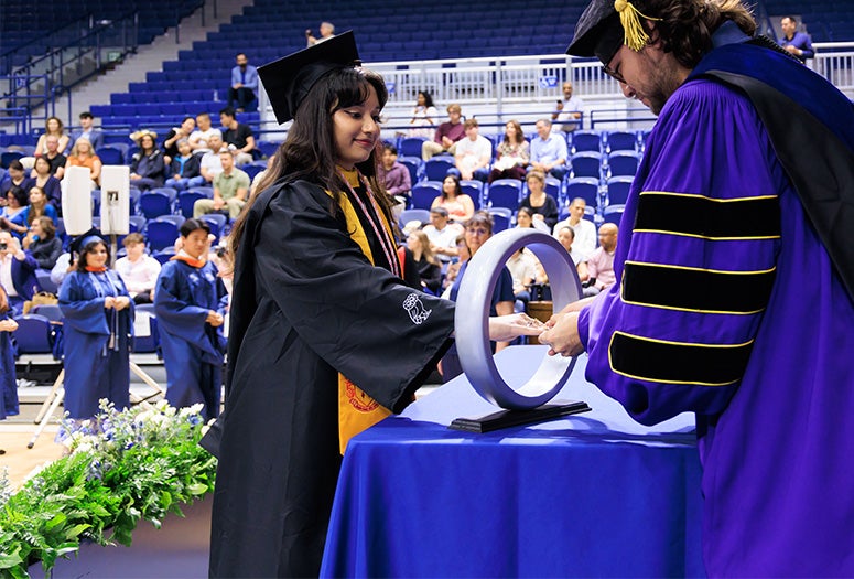 student in academic robes receives ring from professor