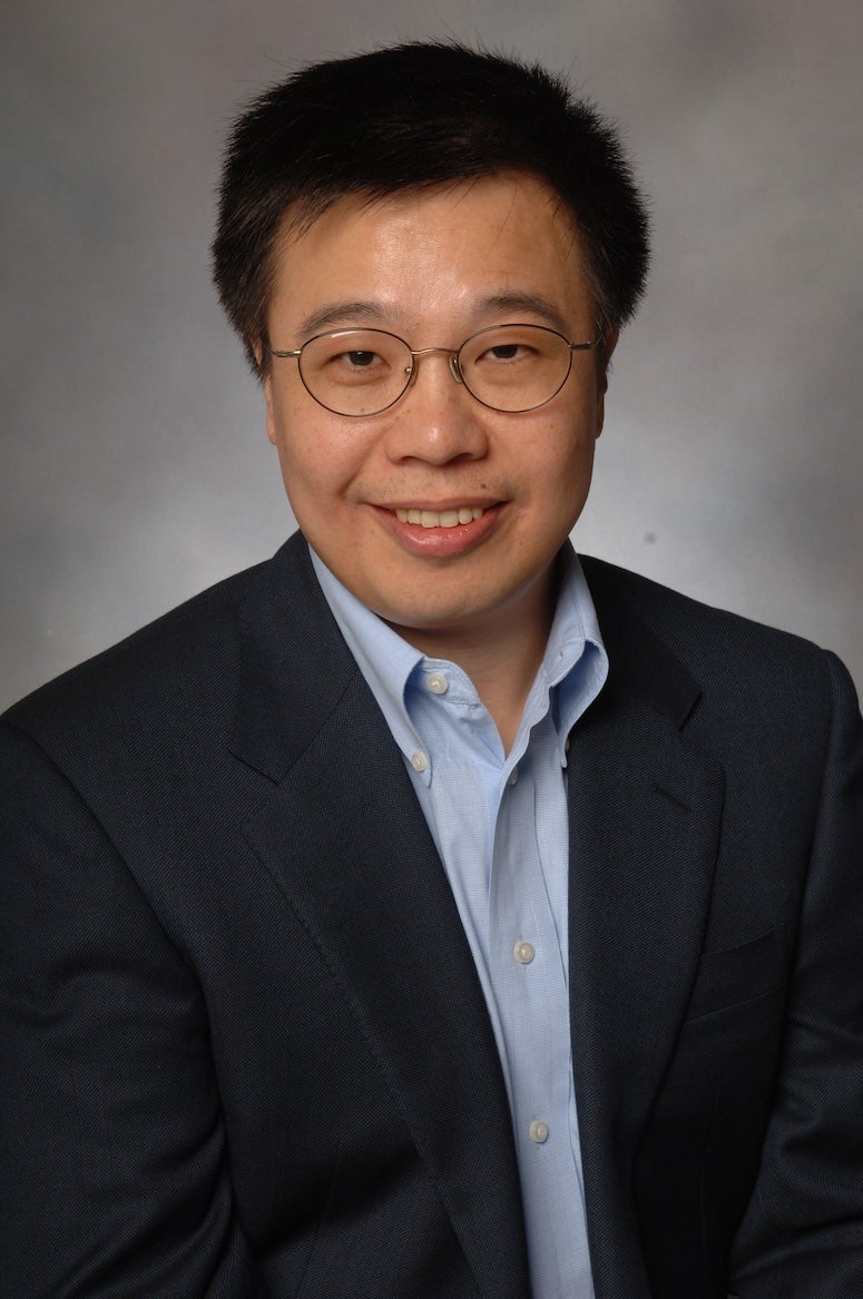 An Asian man in a suit smiles at the camera