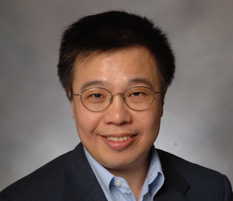 A Chinese man in glasses smiles at the camera