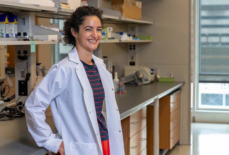 female researcher in lab coat leaning against lab bench