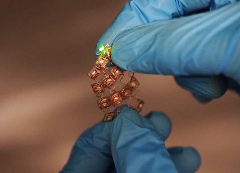 Stretchable moisture-activated battery held by two blue-gloved hands