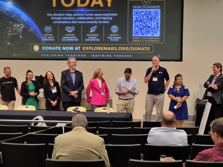 A group of people stand in front of an audience, talking and laughing. 