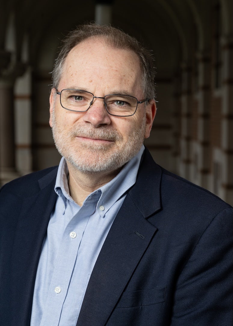 An older white man in a suit smiles gently at the camera. 
