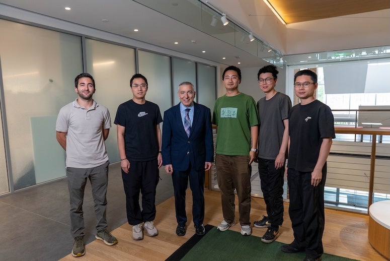 An older white man stands with five young Asian men. 