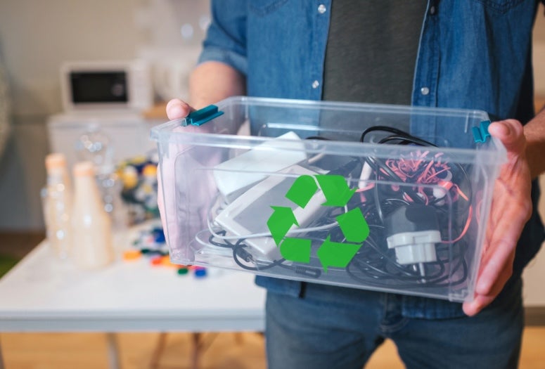 A white person holds a plastic bin full of electronic waste. 