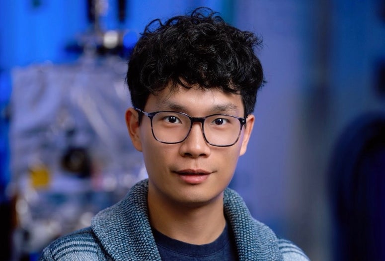 An Asian man in glasses smiles slightly.