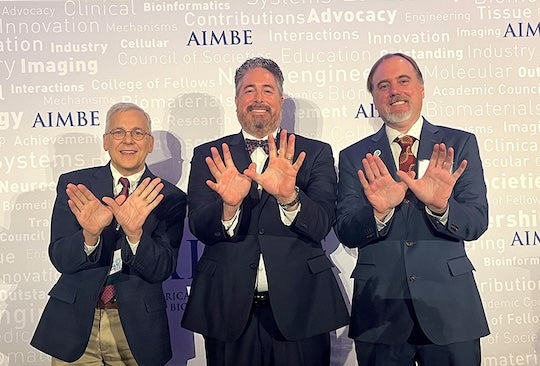 three men facing the camera and holding the owl sign