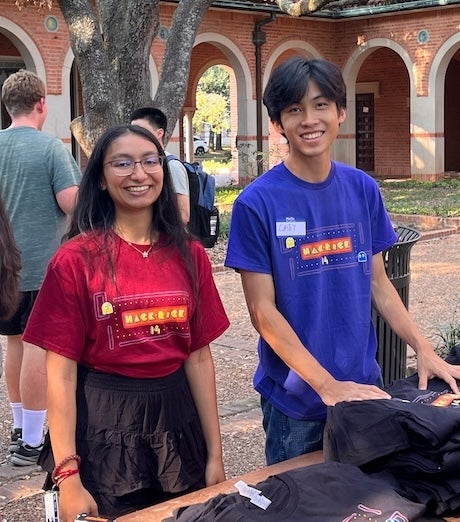 a young woman and young man wearing 'hack Rice' t-shirts smile at the camera 