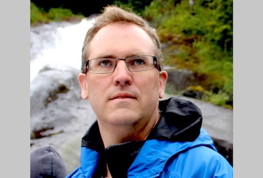 headshot of man with glasses against nature backdrop