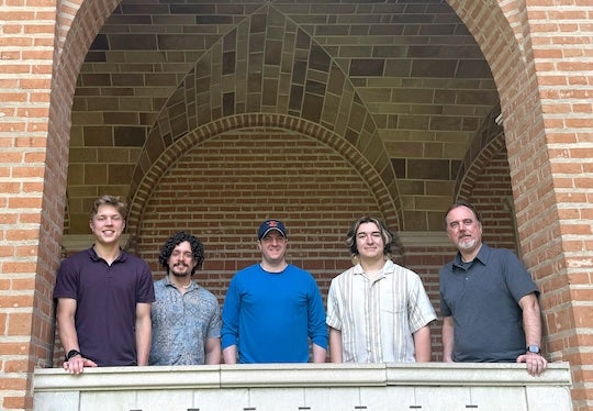 5 male researchers stand inside brick arch