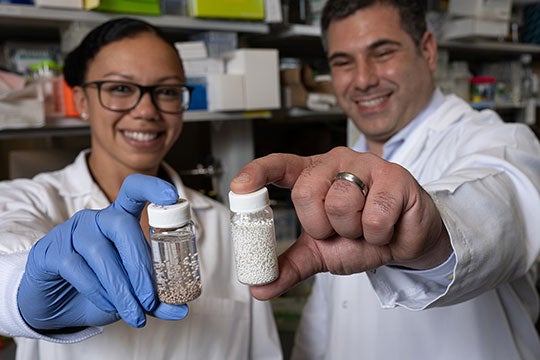 Rice University bioengineers Amanda Nash and Omid Veiseh with vials of bead-like “drug factories” they created to treat cancer