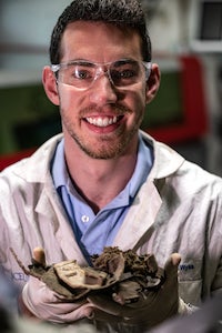 Rice University graduate student Kevin Wyss holds muddy parts from an “end-of-life” truck disassembled in a Ford stripping yard. The Rice lab worked with Ford to recycle plastic parts into graphene that would be used to enhance polyurethane for new vehicles. (Credit: Jeff Fitlow/Rice University)