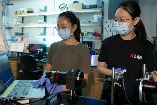 Rice University graduate students Faye Yap, left, and Zhen Liu characterize a mask sample. Researchers at Rice and the University of Texas Medical Branch, Galveston, have established a framework for properly decontaminating disposable facemasks. They determined that heating a mask in a 160-degrees-Fahrenheit oven for five minutes kills more than 99.9% of the viruses they tested, including SARS-CoV-2. (Credit: Jeff Fitlow/Rice University)