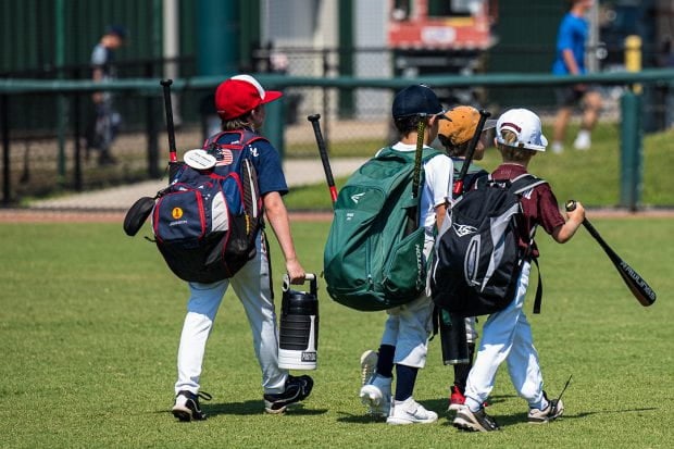 Three boys walking on a baseball field holding equipment
