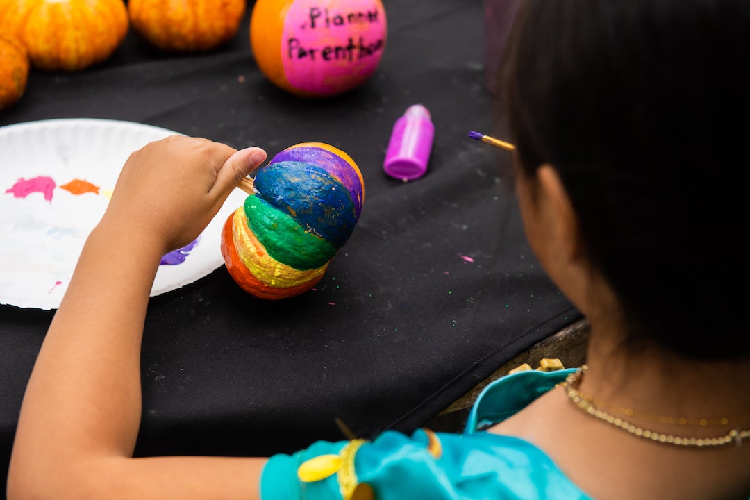 Child painting pumpkin with rainbow colors at Project Pumpkin 2022