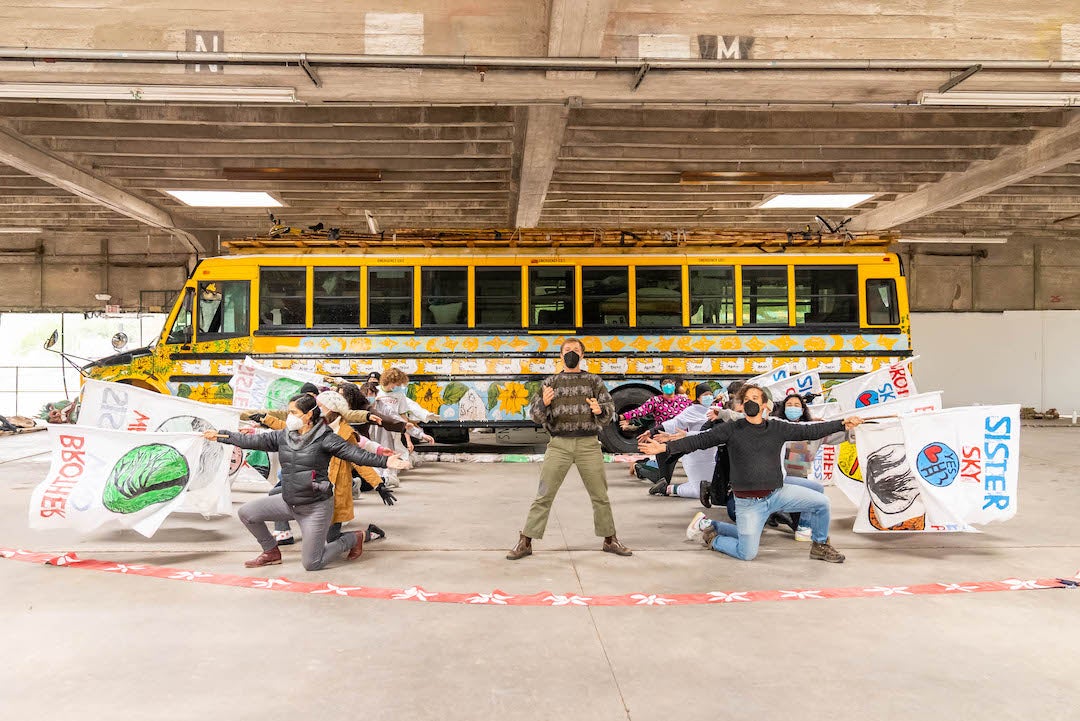 Performers with flags practice in front of school bus