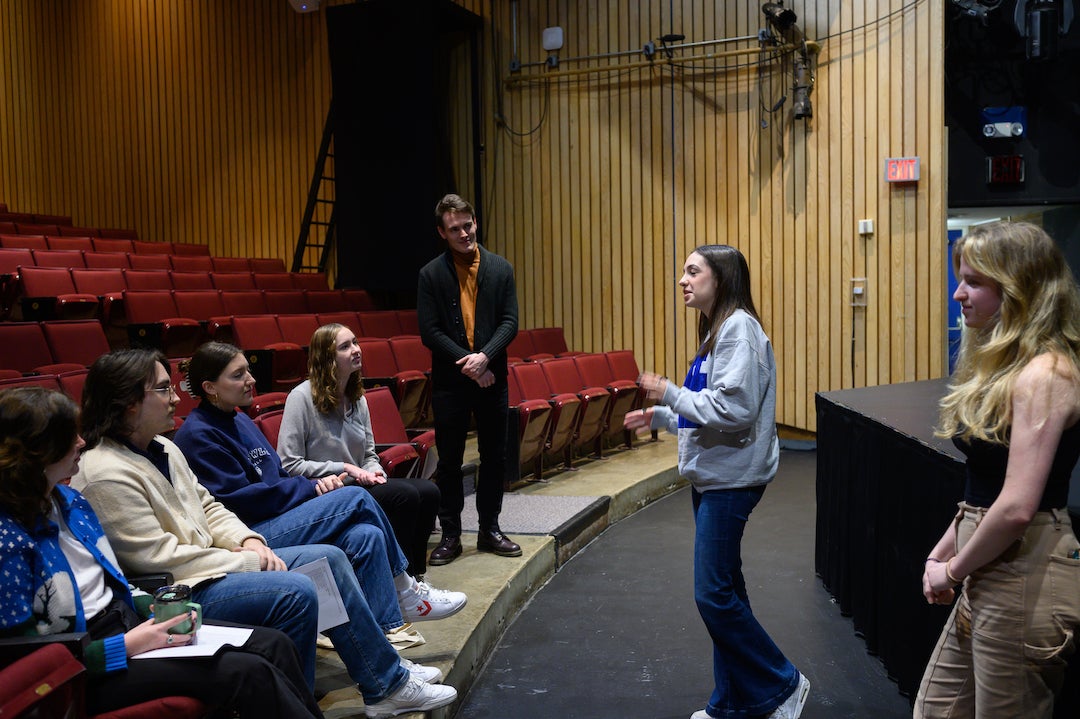 Students and actors taking part in acting workshop while students speak and others sit in theater chairs