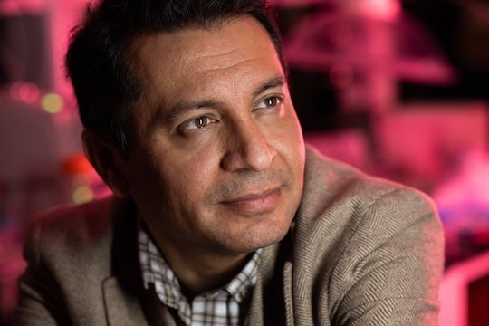 Man looking off camera into the distance, against a background bathed in soft pink light