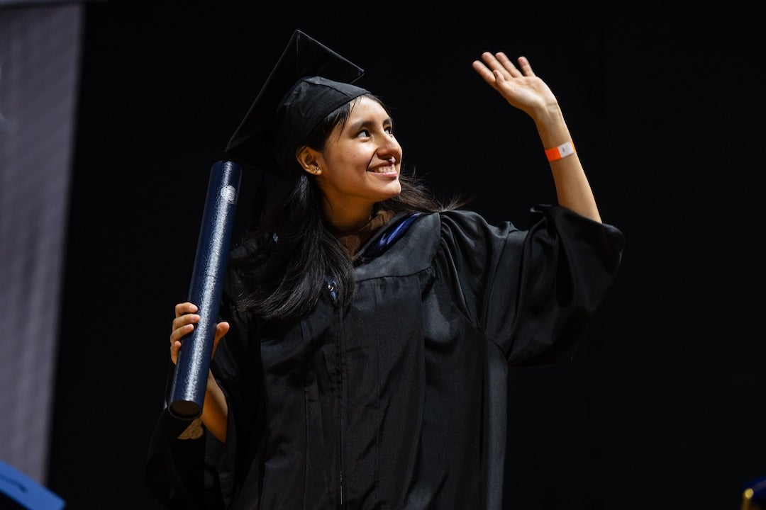 A female graduate waves to the crowd after receiving her diploma.
