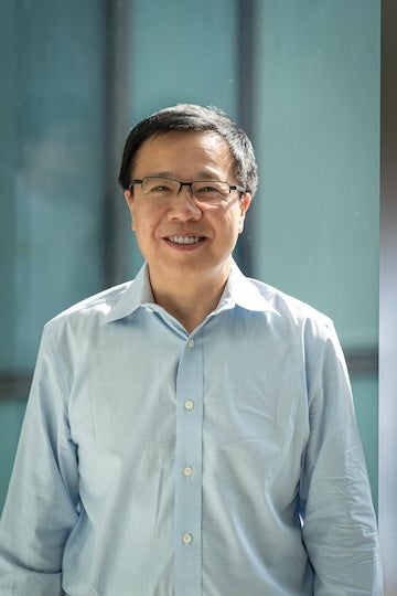 A middle aged East Asian man stands outside smiling at the camera