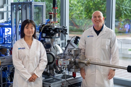 a female and male researcher stand on either side of a pulsed laser deposition device