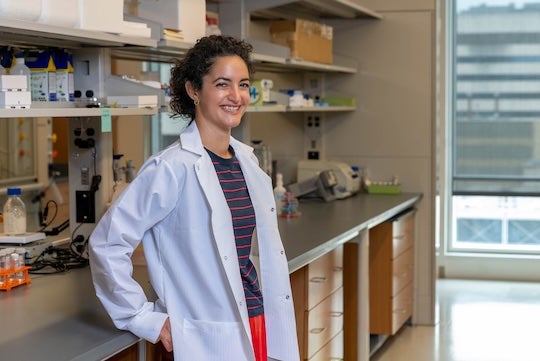 smiling woman in lab coat leaning against bench in lab