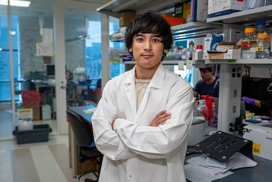 male researcher in lab wearing lab coat poses for the camera