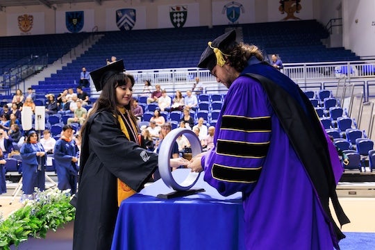student in academic robes receiving ceremonial ring