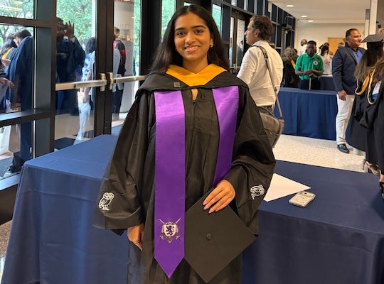 student in academic regalia smiles at the camera