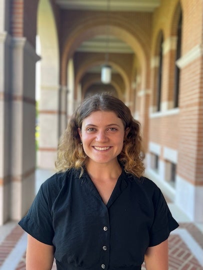 A white woman stands in an outdoor hallway smiling at the camera.